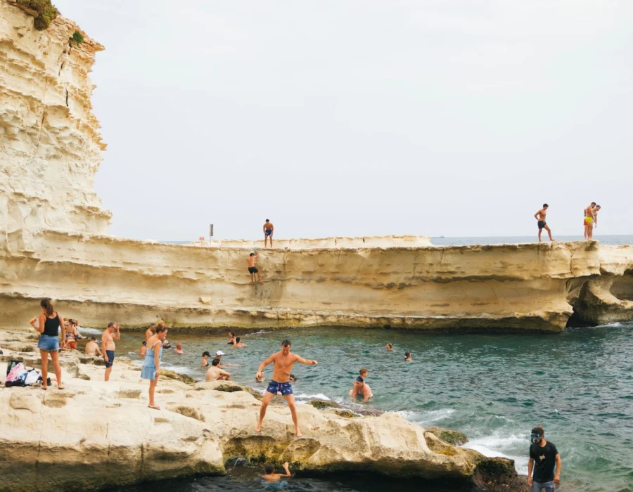 People swimming and jumping into clear water from rocks