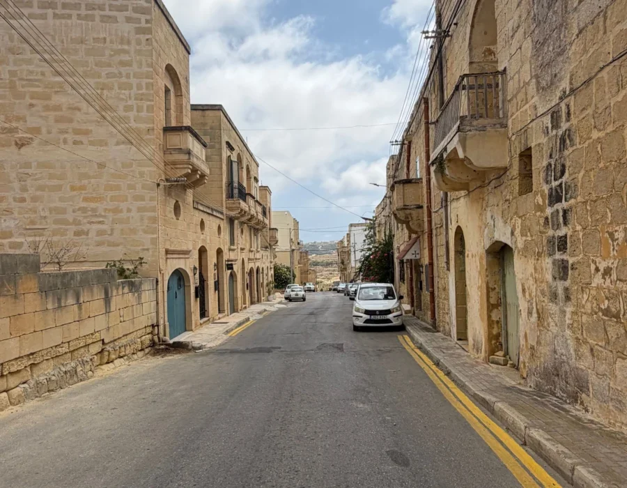 A narrow street in a Maltese village, one car wide with parking on both sides