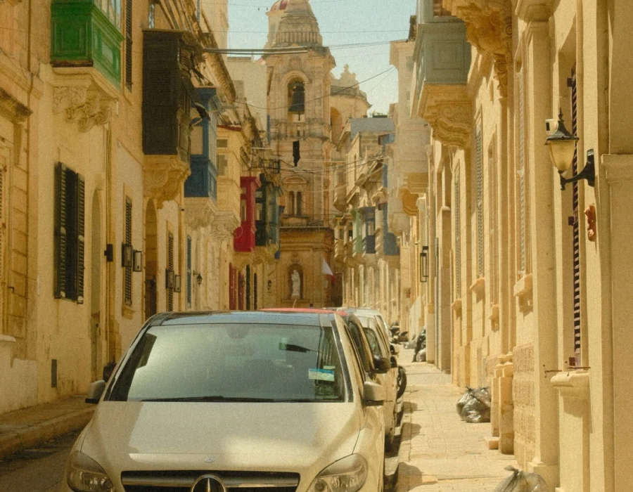 A sunny Maltese street with cars and a church behind