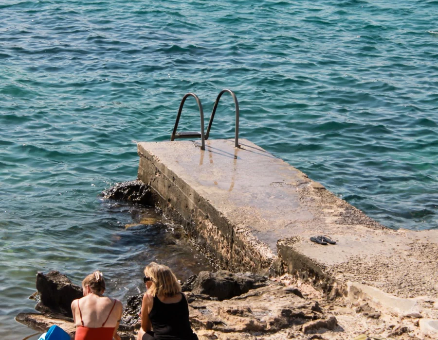 Two people sitting on a stone pier above clear turquoise water at Sliema